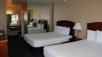 A hotel room with two single beds, a bedside table with a lamp, a mirror, and a view of the outside.
