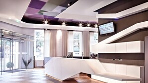 A modern hotel lobby with a reception desk, glass doors, and a large window with curtains. - BoutiqueHOTEL Donauwalzer (Vienna)