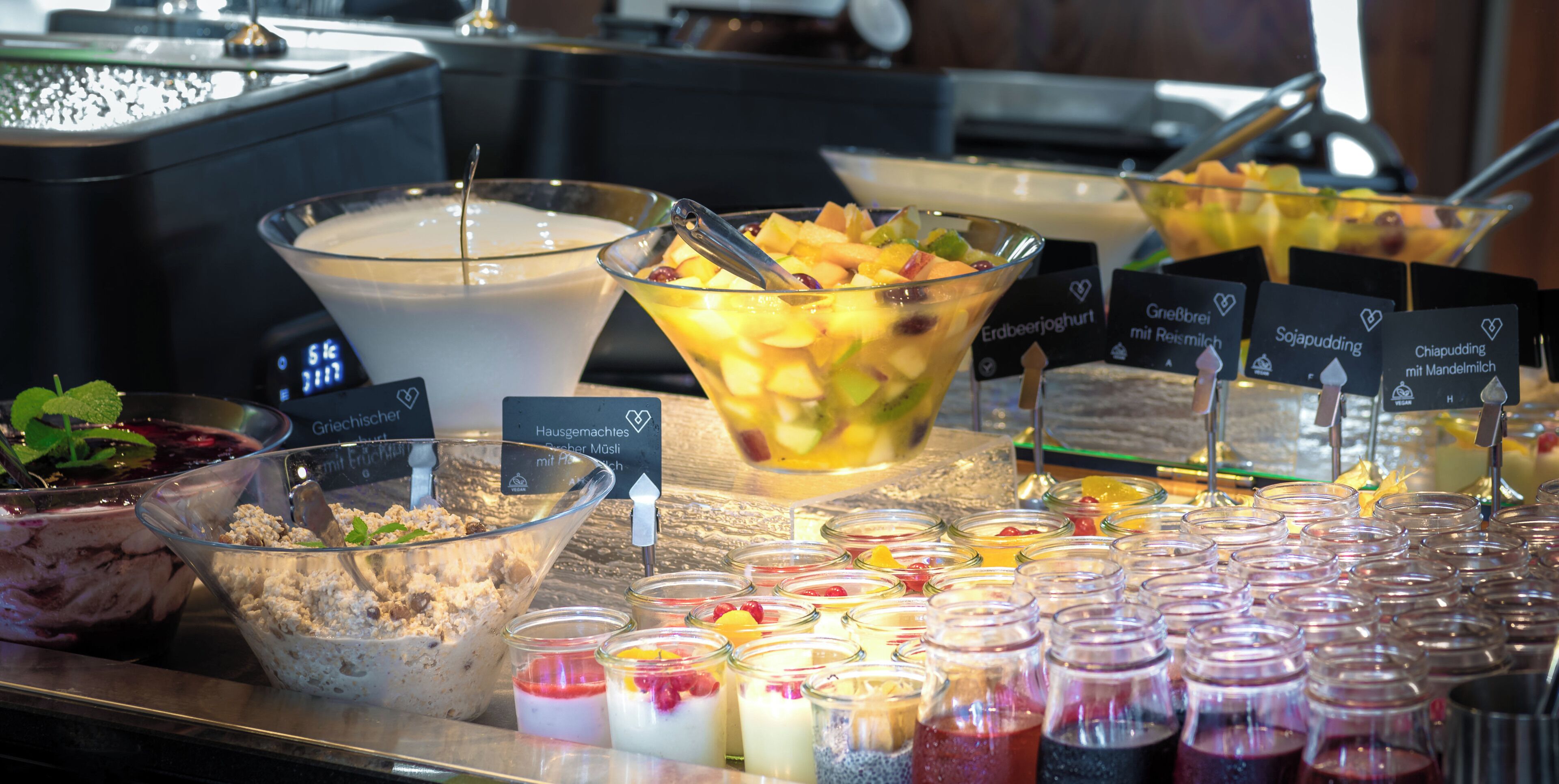 A buffet with various food options including a large bowl of fruit salad, a bowl of yogurt, and multiple small jars of different sauces.