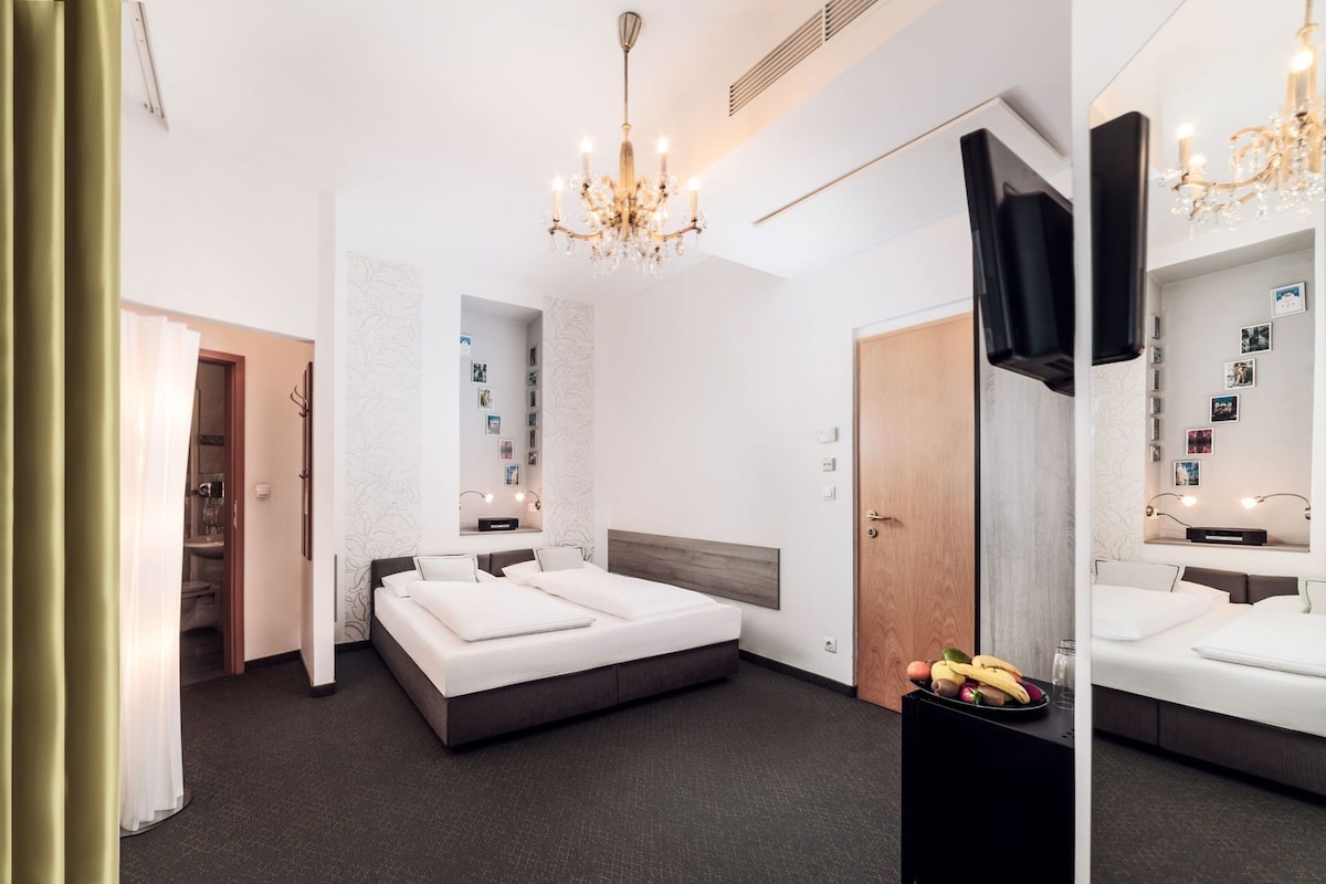 A modern hotel room with a large bed, a desk, a wardrobe, and a chandelier.