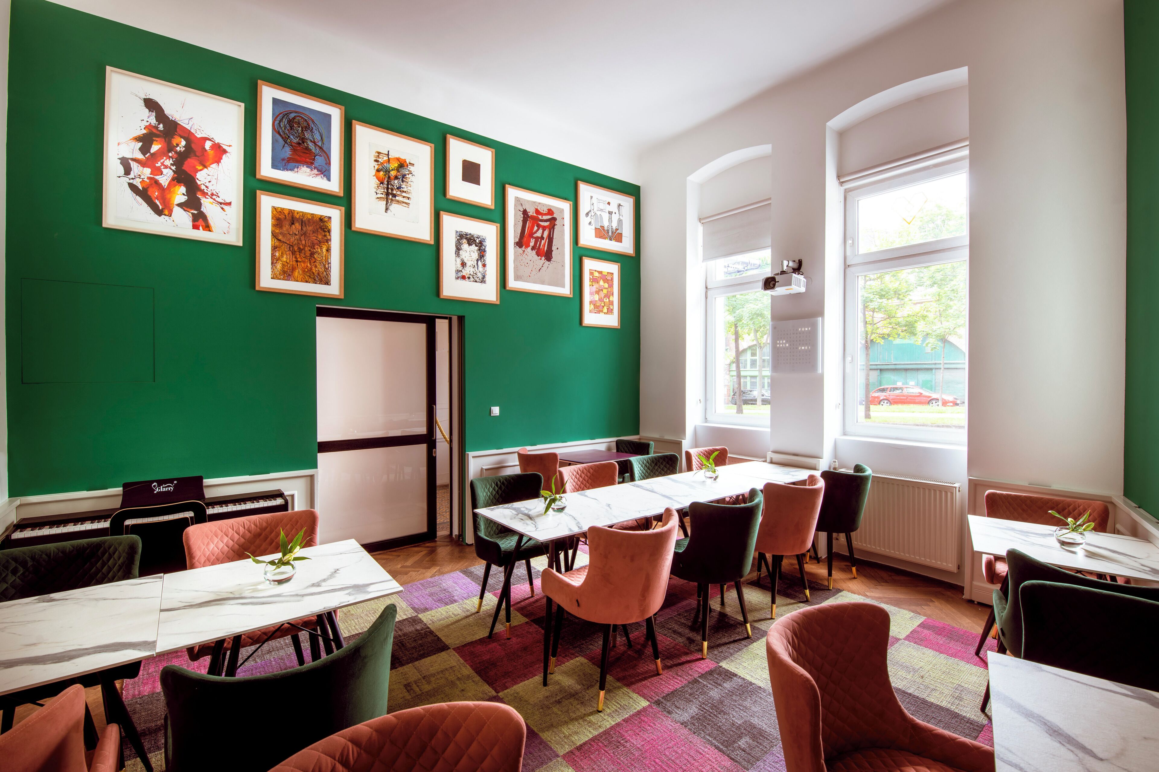A dining area with a green wall, multiple framed artworks, and a large window with a view of the outside.