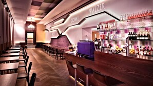 A modern bar area with a long counter, bar stools, and a variety of bottles and glasses on shelves. - BoutiqueHOTEL Donauwalzer (Vienna)