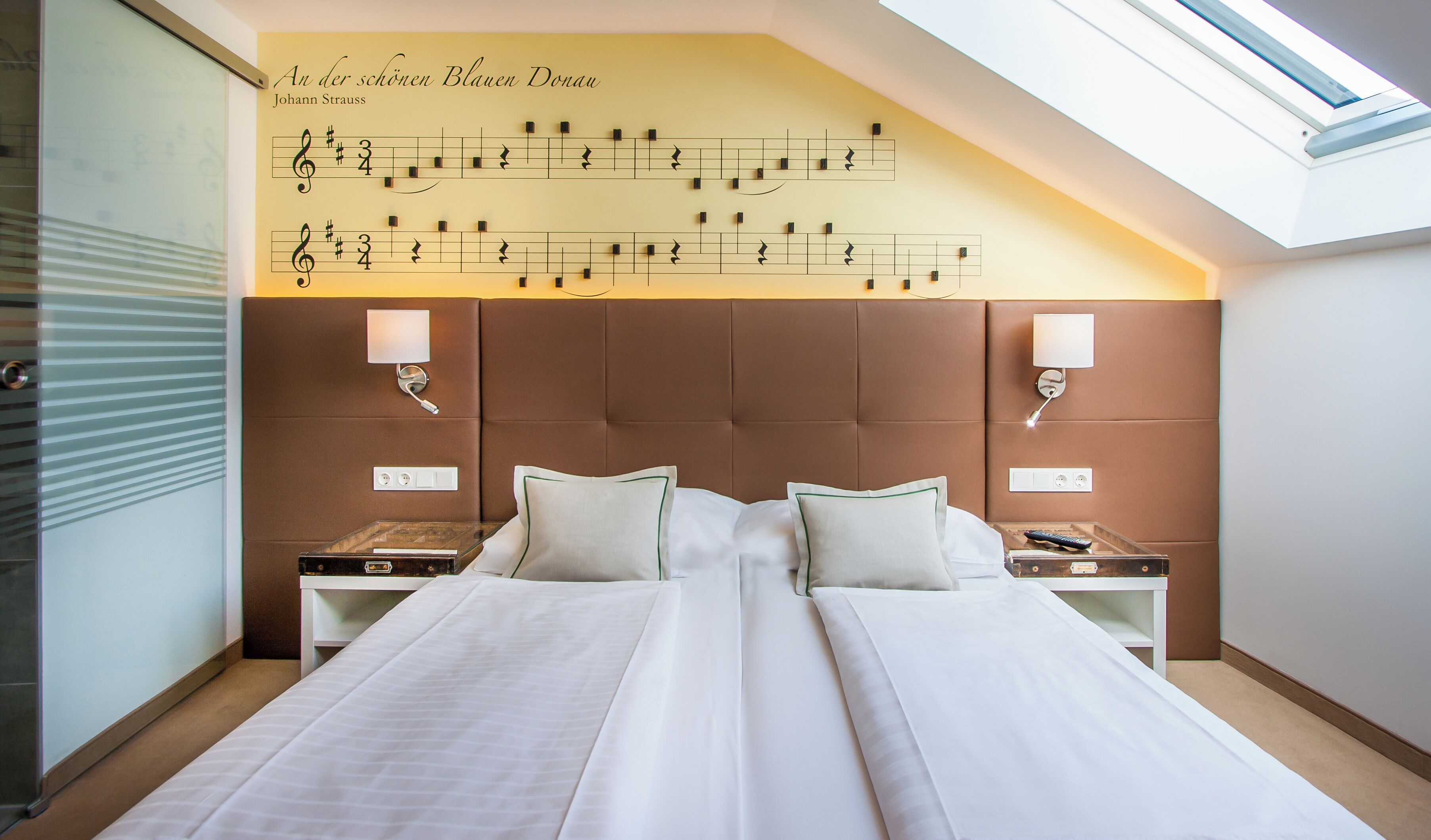 A hotel room with a large bed, two bedside tables, a wall-mounted lamp, and a skylight.