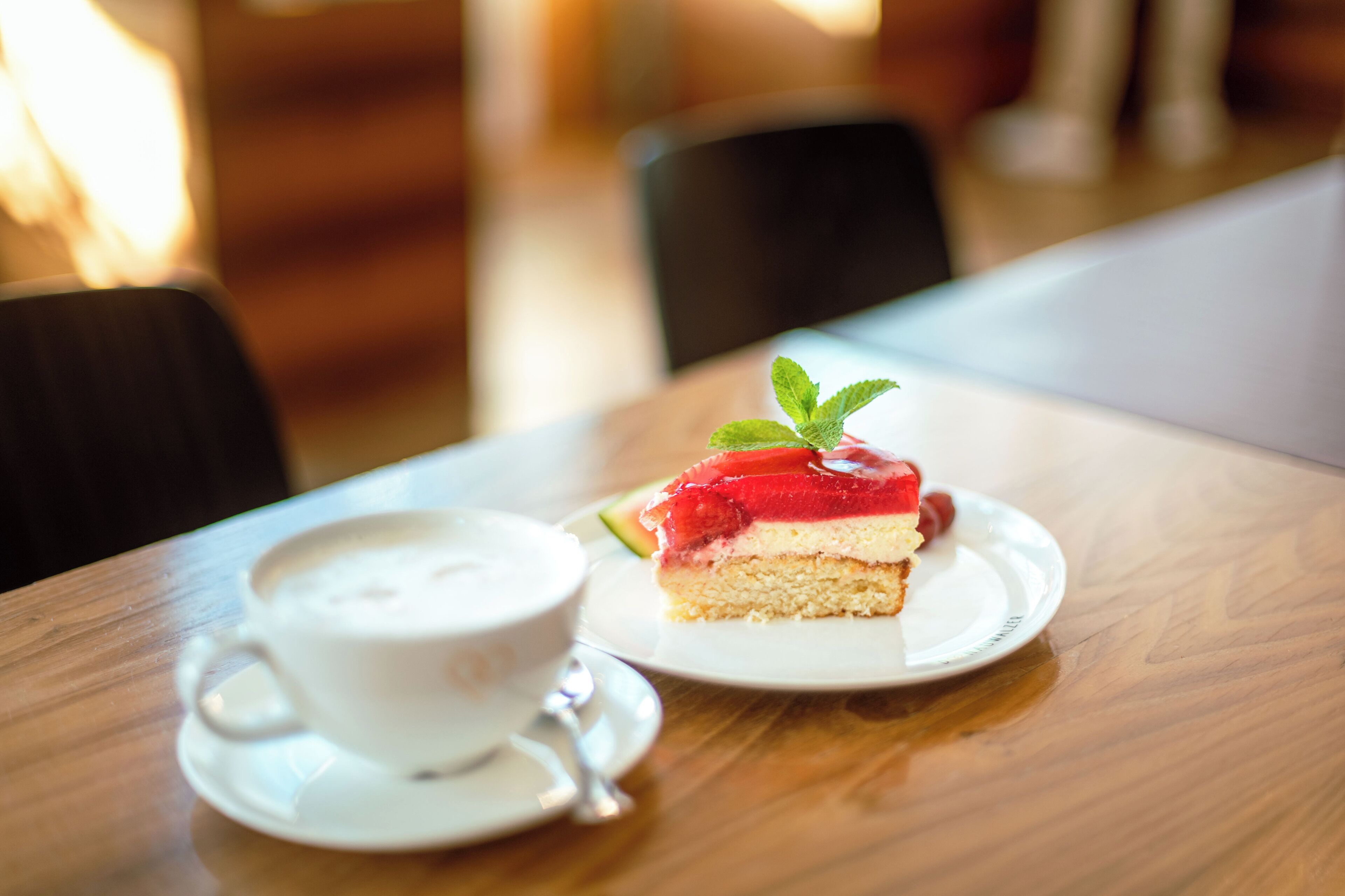 A slice of layered dessert on a plate with a mint garnish, next to a cup of coffee on a saucer.
