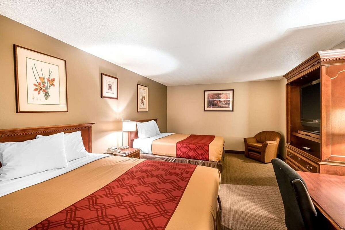 A hotel room with two beds, a desk, a chair, a television, and framed artwork on the walls.