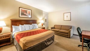 A hotel room with a bed, a desk, a chair, a couch, and two framed pictures on the walls. - Holiday Lodge Yakima (Yakima)