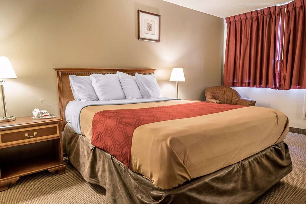 A hotel room with a bed, two bedside tables, a chair, a window with curtains, and a framed picture on the wall.