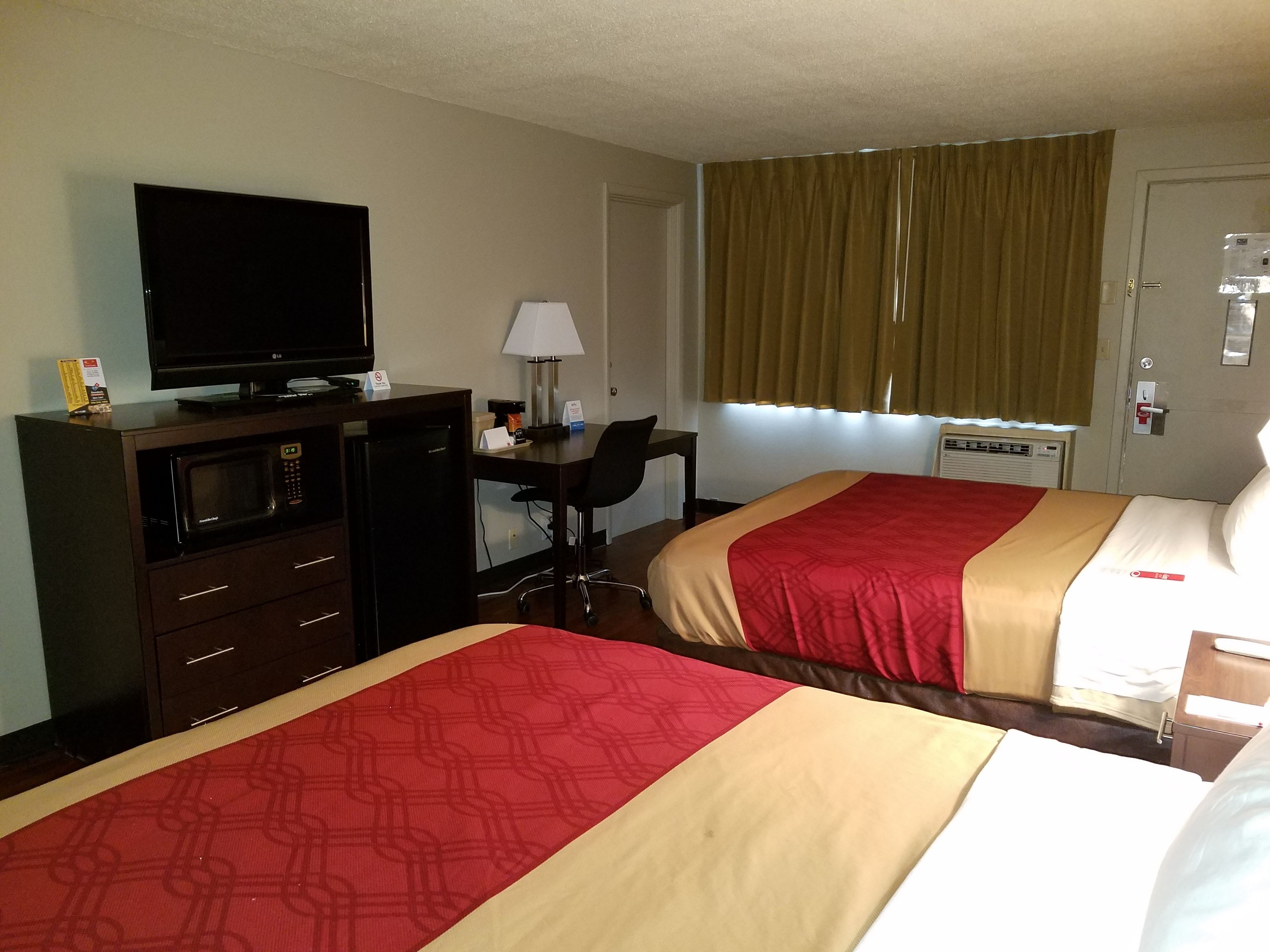 A hotel room with two beds, a TV, a desk, a lamp, and a window with curtains.
