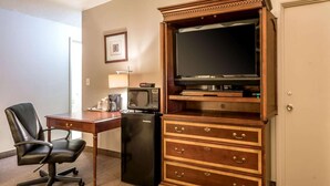 A hotel room with a wooden desk, a black office chair, a black refrigerator, a microwave, a television on a wooden stand, and a wooden dresser with drawers. - Holiday Lodge Yakima (Yakima)