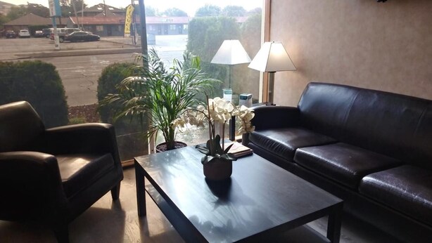 A room with a leather sofa, a coffee table with a plant, and a view of a parking lot through a window. - Holiday Lodge Yakima (Yakima)