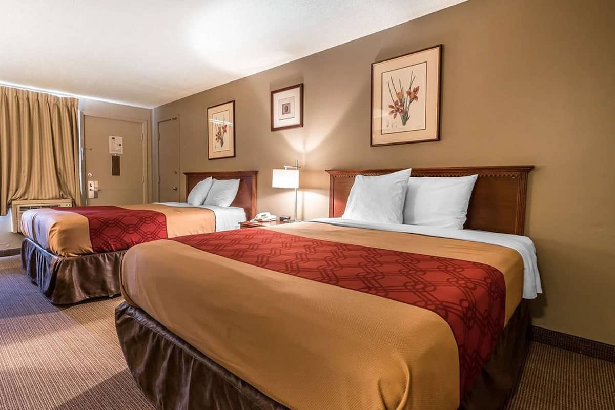 A hotel room with two beds, beige walls, and framed floral artwork.