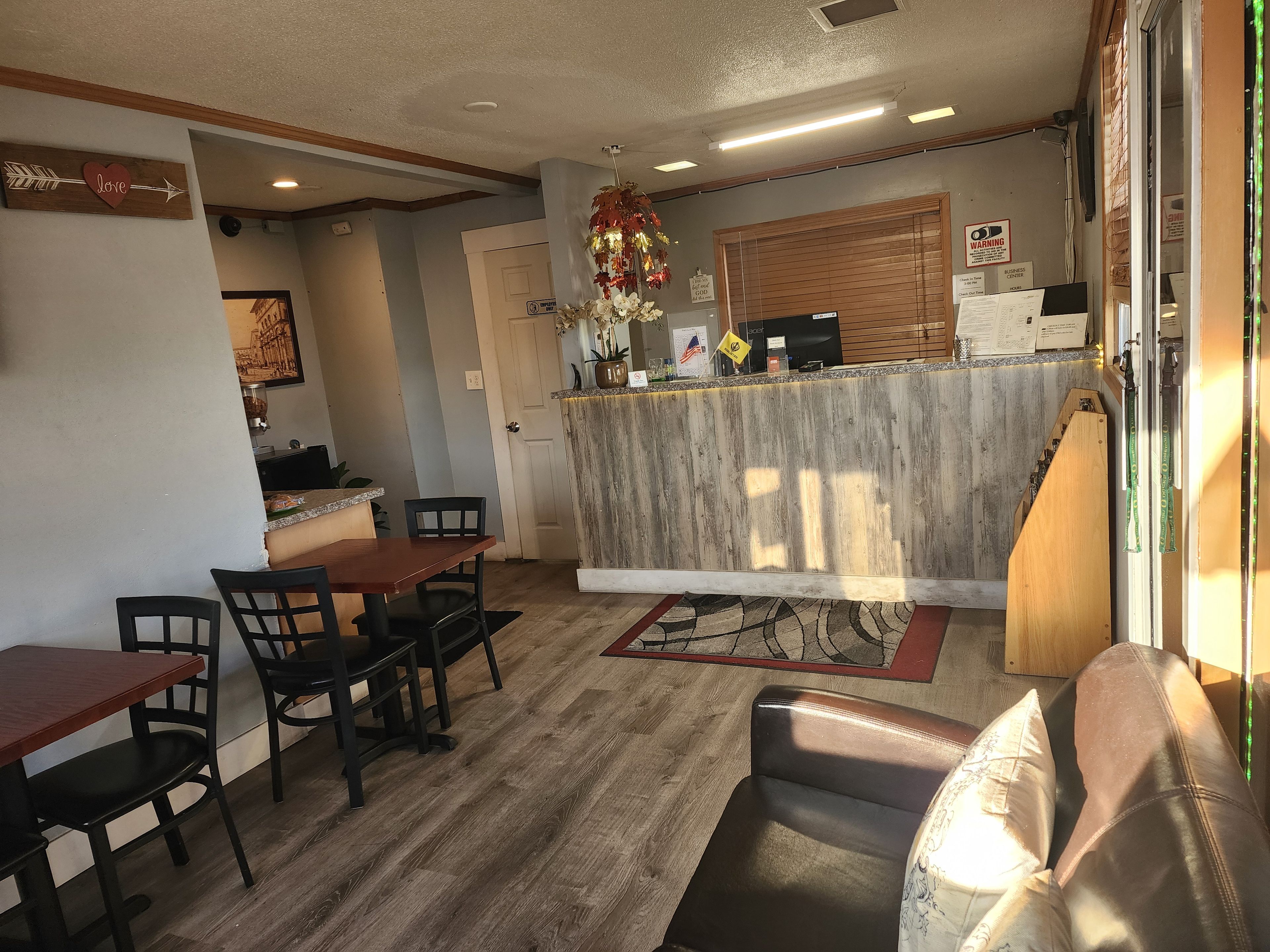 Un comedor con mesa y sillas de madera, una recepción con un ordenador y una ventana con persianas.