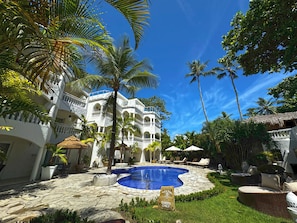A resort with a swimming pool, palm trees, and a white building with balconies. - Hotel Villa Taina (Cabarete)