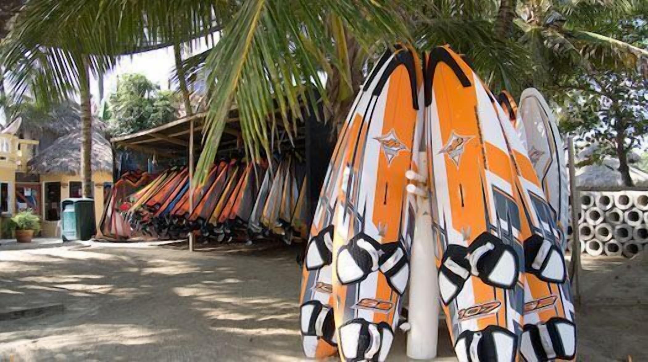 Surfboards leaning against a wall in a shaded area with a building in the background.