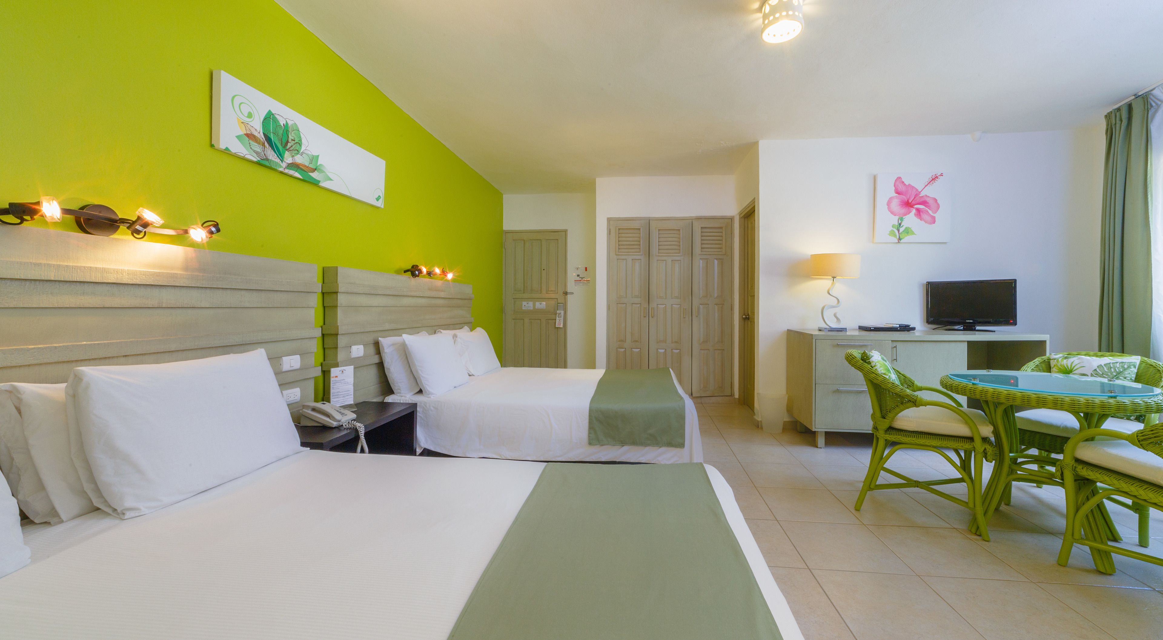 Een hotelkamer met twee bedden, een bureau met stoel, een televisie en kunstwerken aan de wanden.