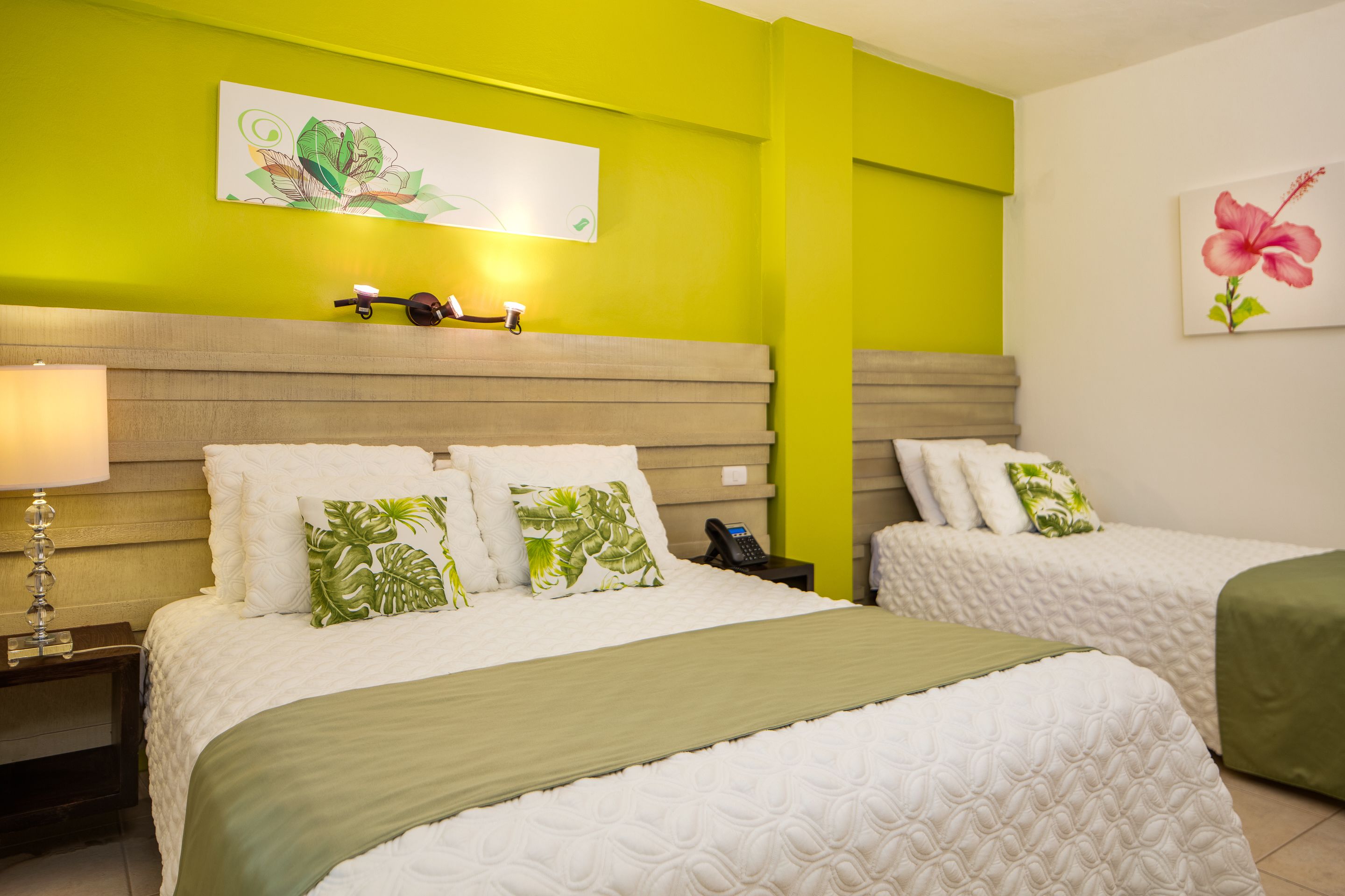 Quarto de hotel com duas camas, uma mesa de cabeceira com abajur e obras de arte nas paredes.