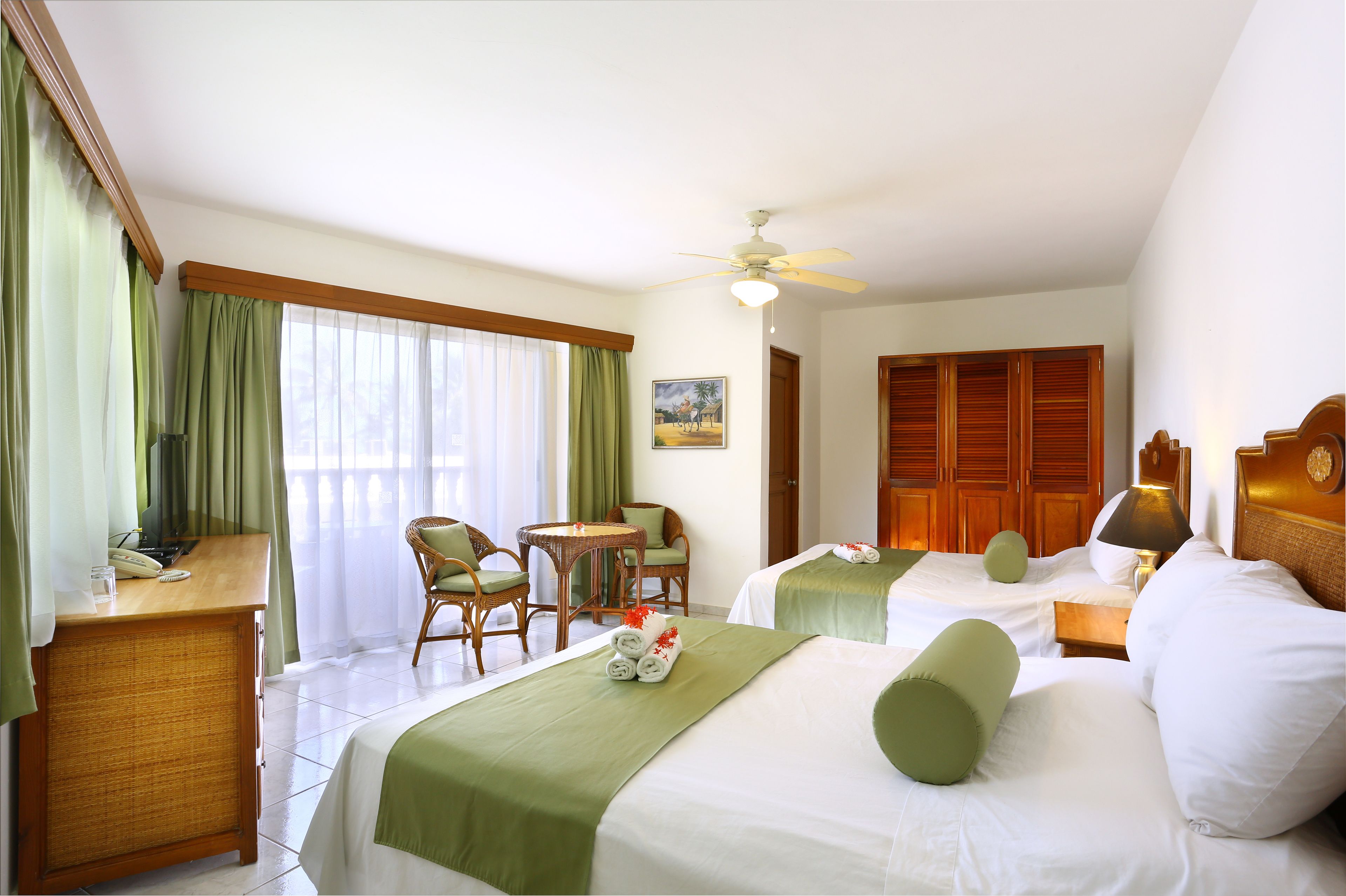 Habitació d'hotel amb dos llits, un escriptori amb telèfon, una cadira, una taula i un ventilador de sostre.
