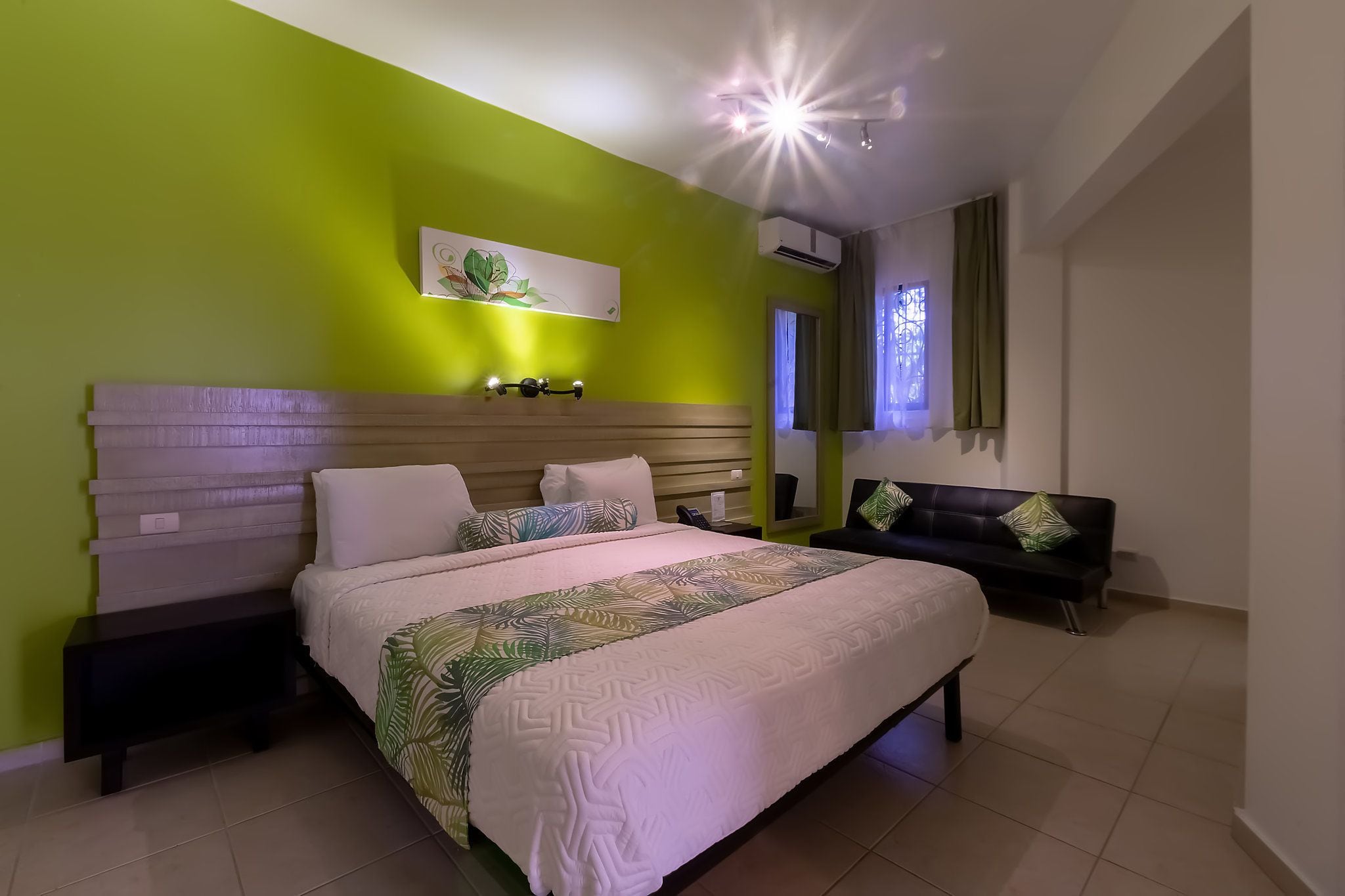 Une chambre à coucher comprenant un lit, des tables de chevet, une tête de lit, un banc et un climatiseur fixé au mur.