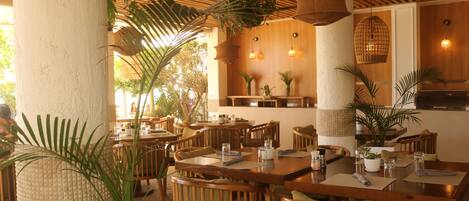 A restaurant with wooden tables and chairs, potted plants, hanging light fixtures, and a wooden ceiling.