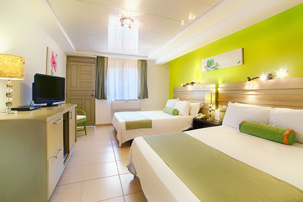A hotel room with two beds, a desk with a television, a chair, and a window with curtains.