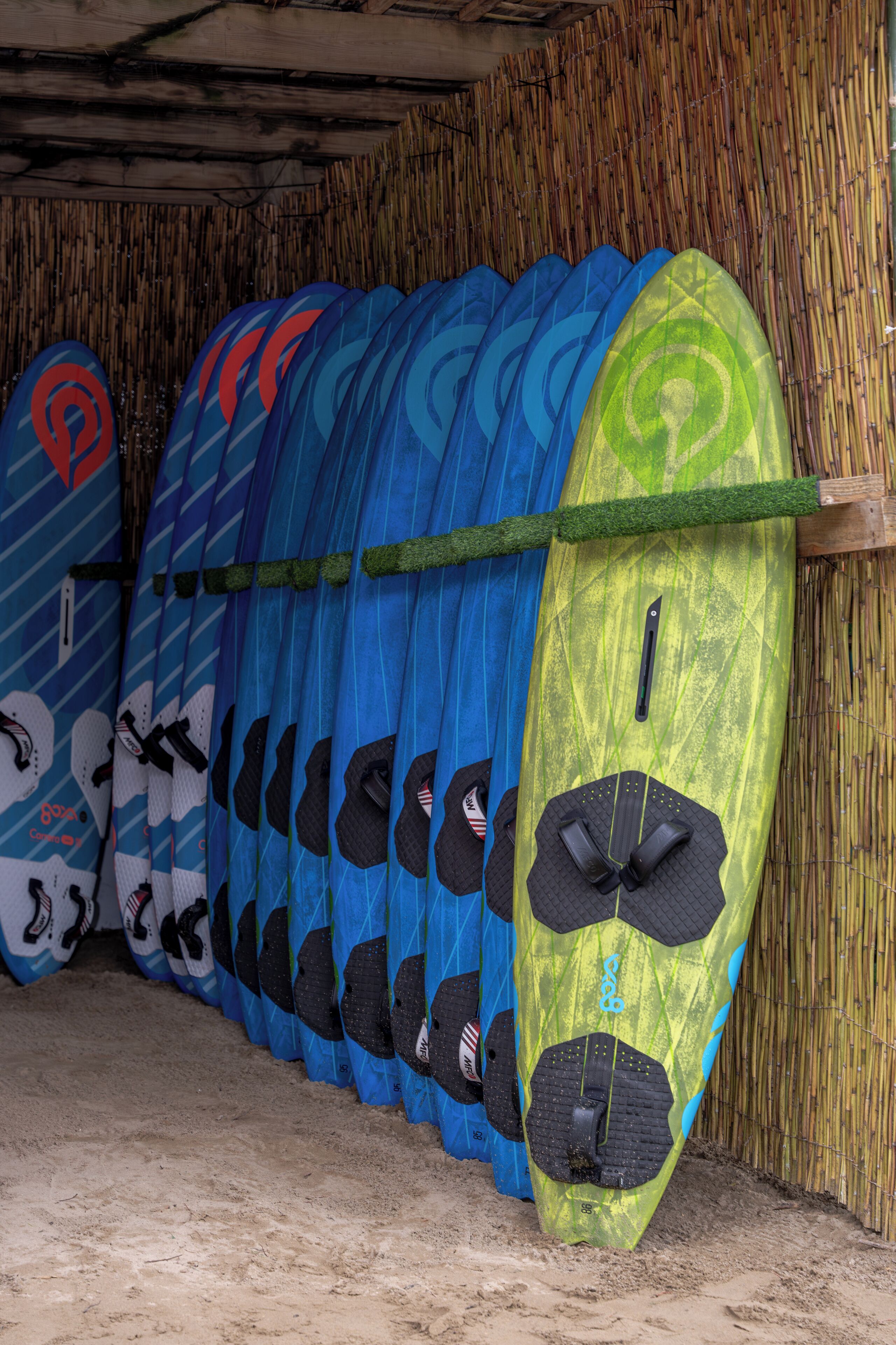 A row of surfboards leaning against a bamboo wall in a covered area.