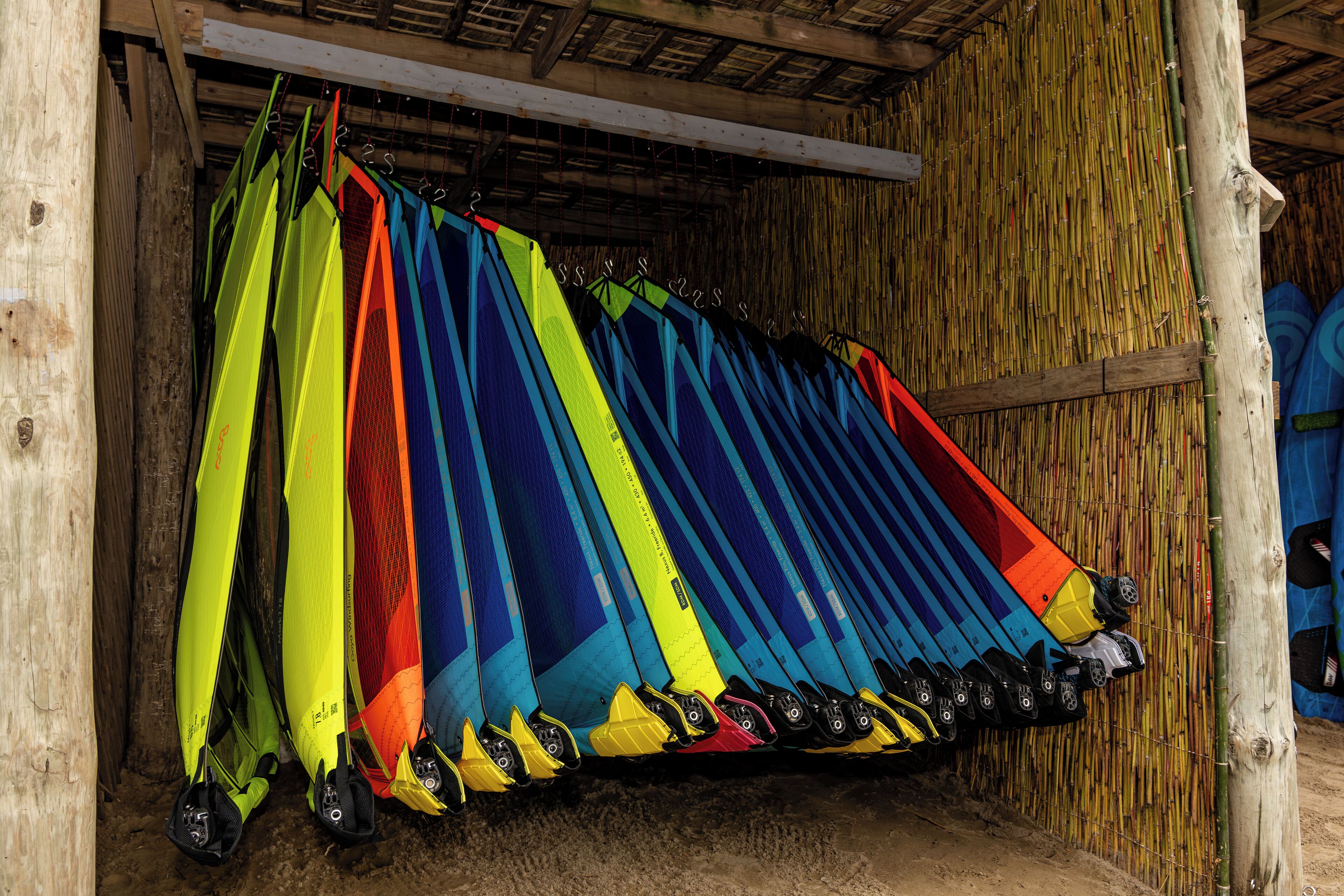 Kayaks de colores colgando frente a una pared de bambú.