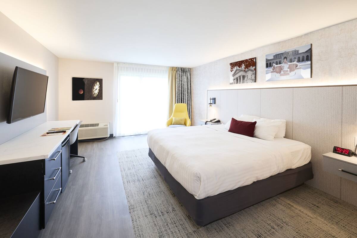 A modern hotel room with a large bed, a desk, a flat-screen TV, and artwork on the walls.