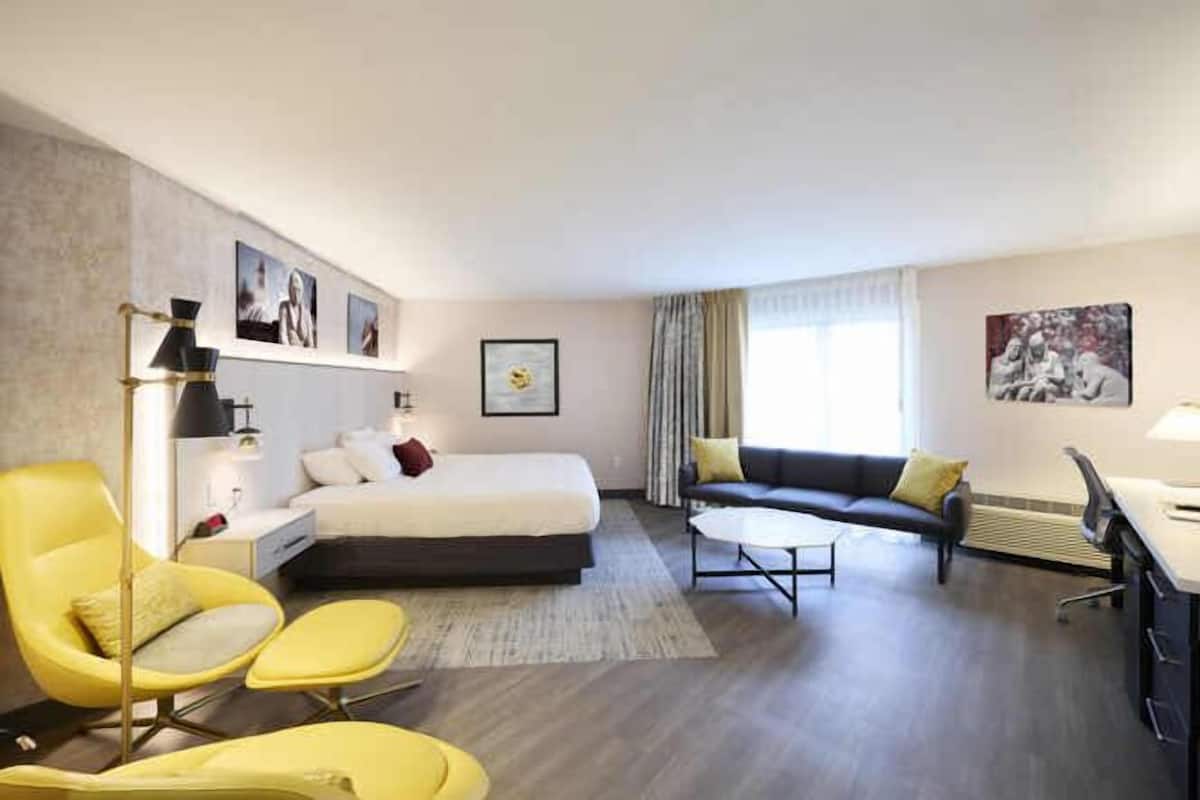 A modern hotel room with a bed, a sofa, a desk, and a chair.