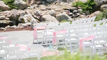 Rows of white chairs with pink sashes, arranged outdoors with a rocky background.