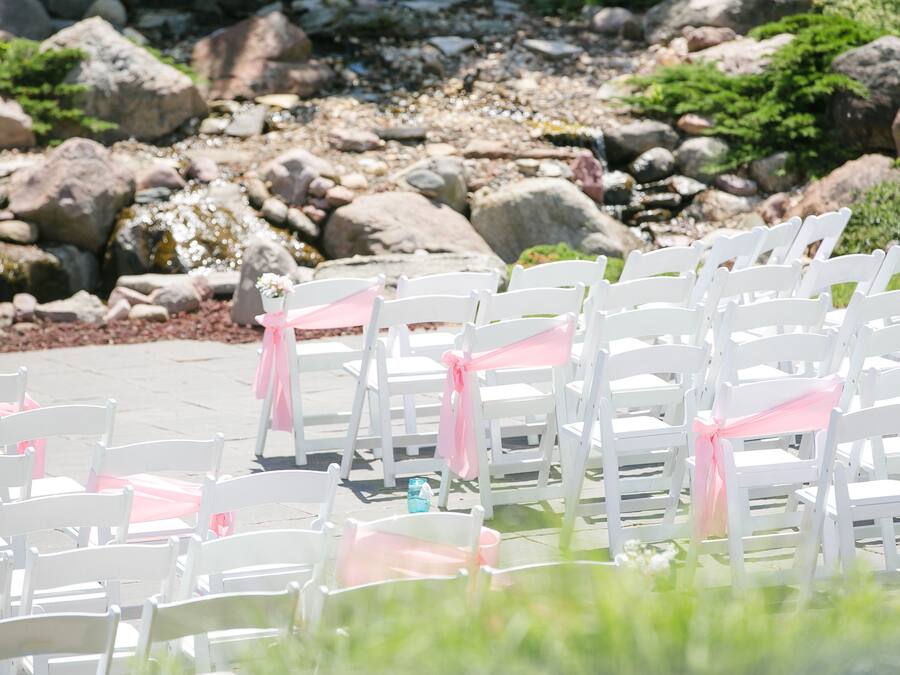 Rows of white chairs with pink sashes, arranged outdoors with a rocky background.