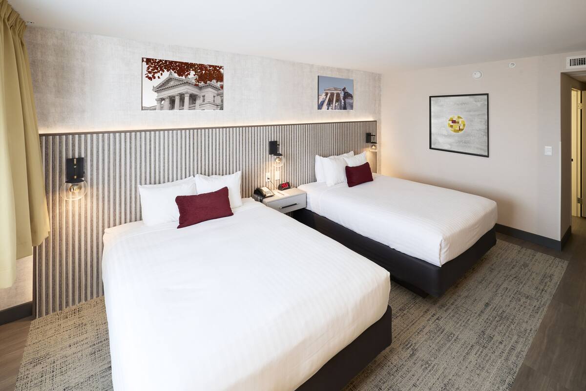 A hotel room with two beds, a striped headboard, and a framed picture on the wall.