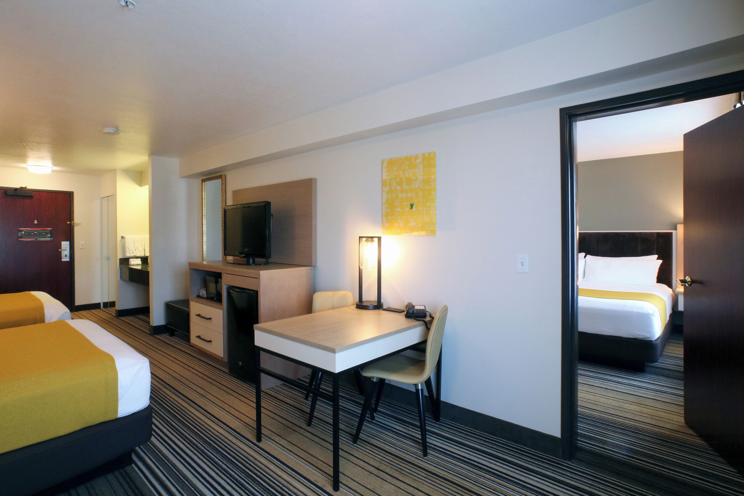 A hotel room with two beds, a desk, a chair, a television, and a mirror.