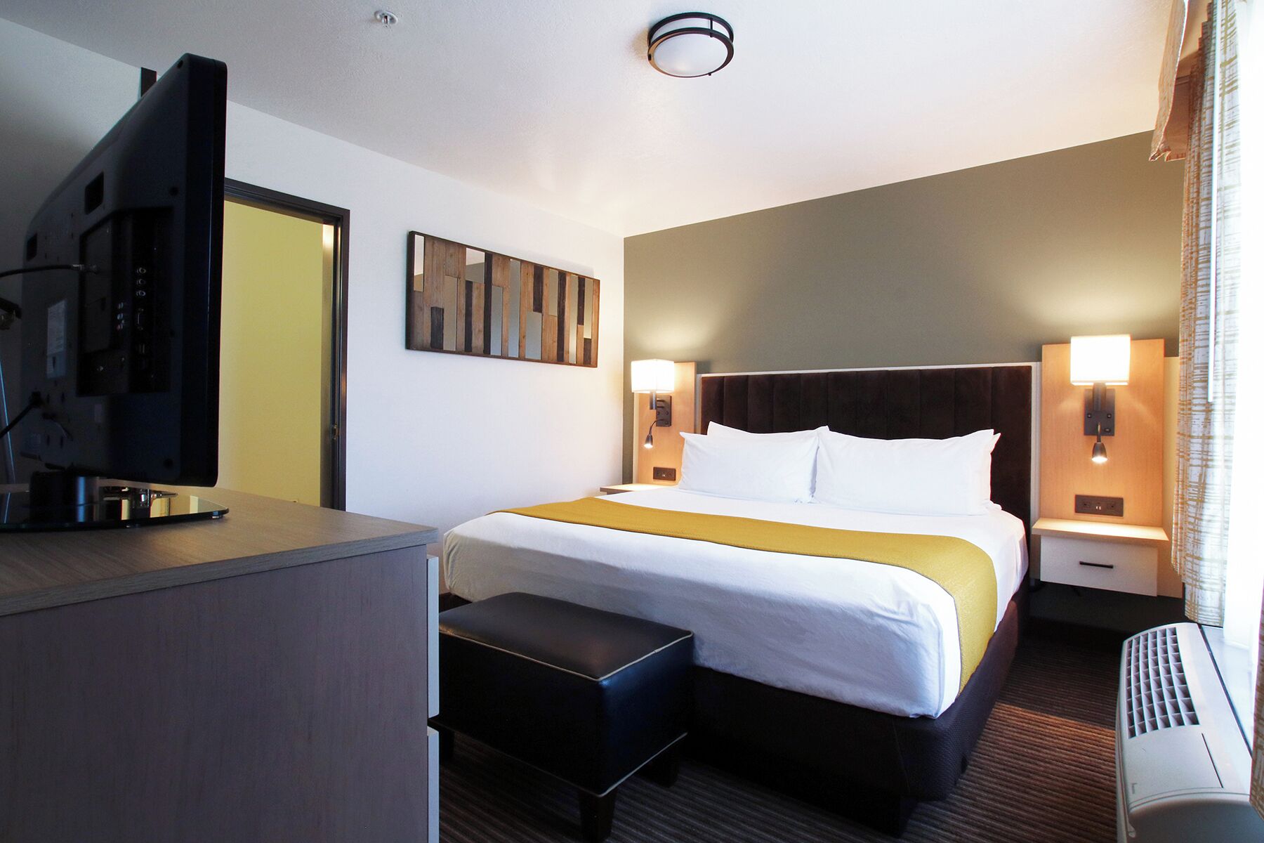 Habitación de hotel con cama, mesitas de noche, escritorio y televisor de pantalla plana, además de una obra de arte colgada en la pared.