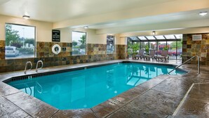 An indoor swimming pool with a lifeguard sign, stone-tiled walls, and a seating area with chairs and a table. - Oxford Suites Spokane Valley (Spokane Valley)