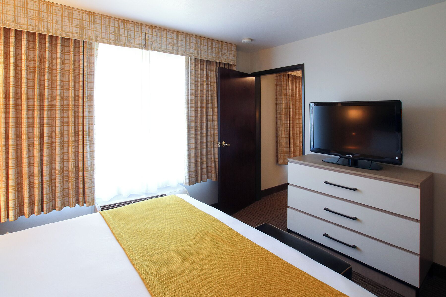 Una habitación de hotel con una cama, un televisor sobre un mueble, un armario y una puerta que da a otra habitación.