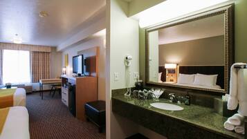 A hotel room with a bed, desk, and a large mirror above the sink.