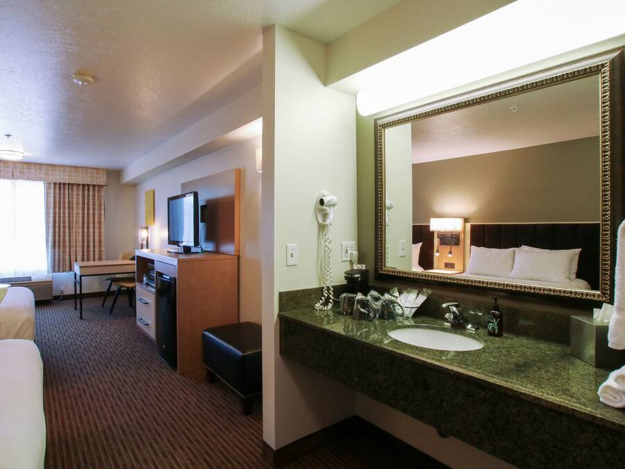 A hotel room with a bed, desk, and a large mirror above the sink.