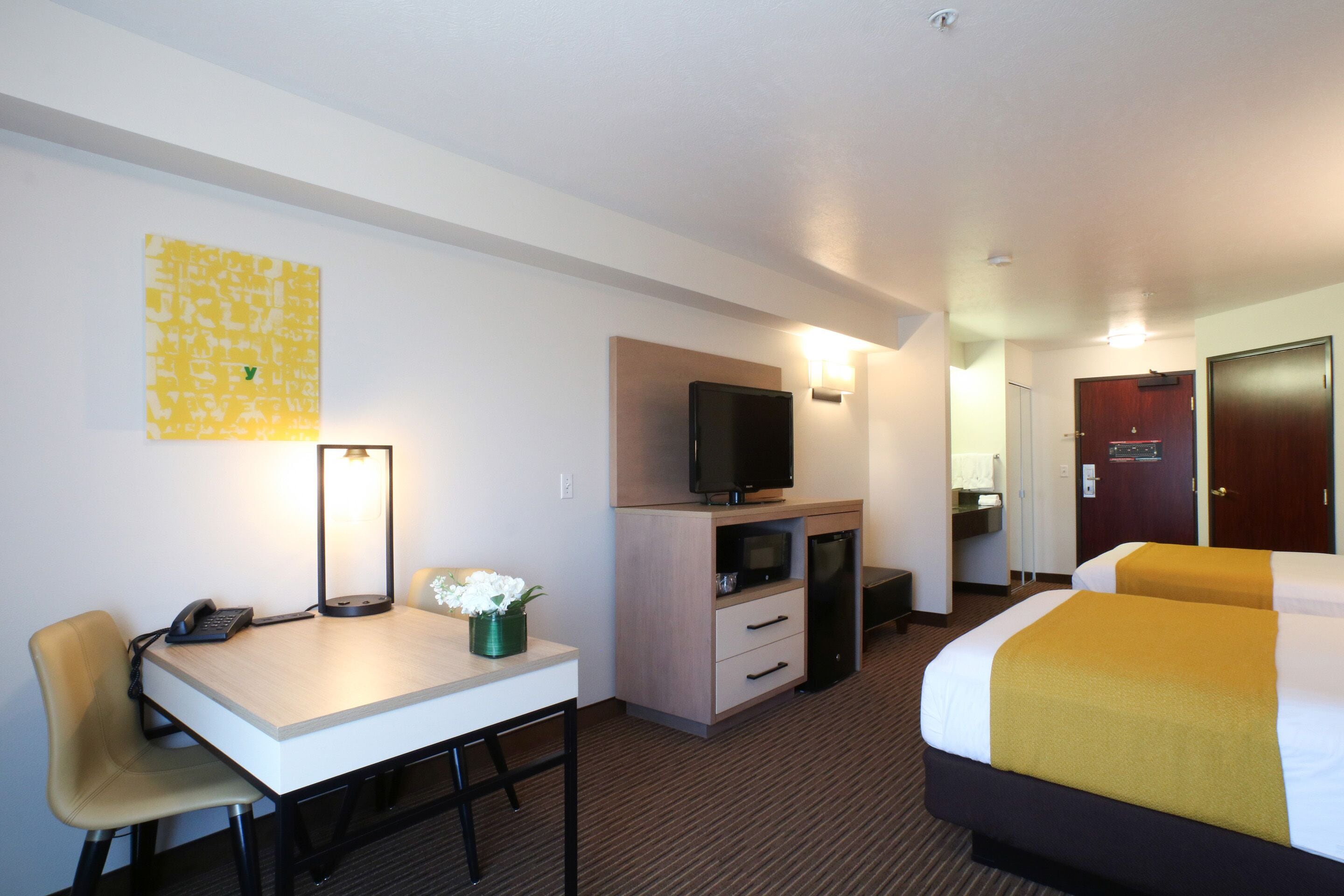 A hotel room with a desk, chair, television, bed, and a small bathroom area.