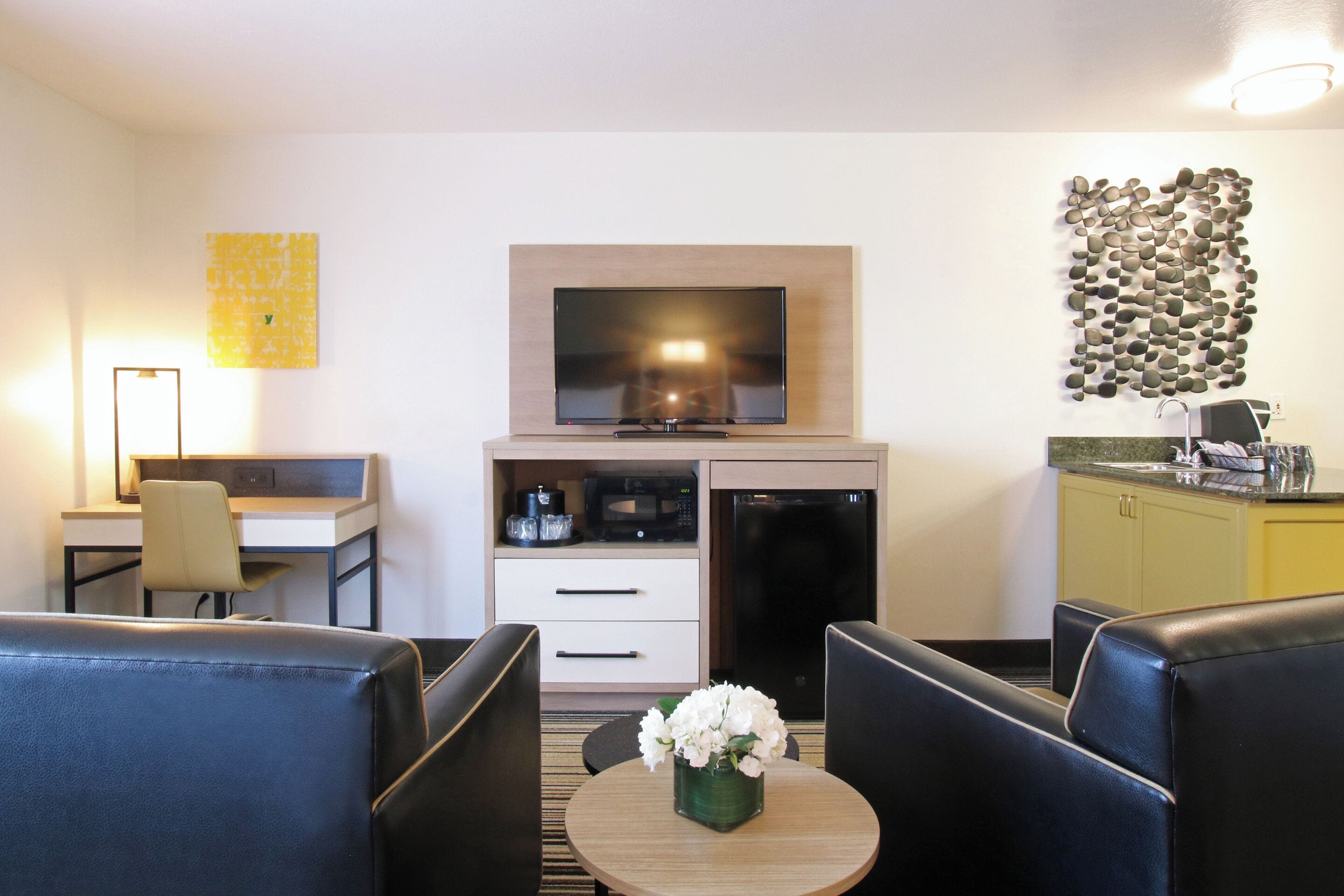 Une chambre d’hôtel compacte dotée d’une télévision à écran plat, d’une petite kitchenette, d’un bureau et d’un coin salon avec deux chaises et une table.