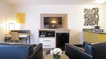 Une chambre d’hôtel compacte dotée d’une télévision à écran plat, d’une petite kitchenette, d’un bureau et d’un coin salon avec deux chaises et une table.