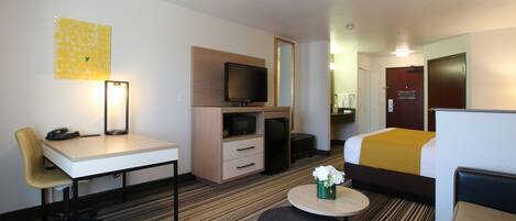 A hotel room with a bed, a desk with a chair, a television, a small table with a vase, and a carpeted floor.