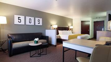 A hotel room with a bed, a sofa, a table, and a desk. There are wall-mounted lamps and a door.