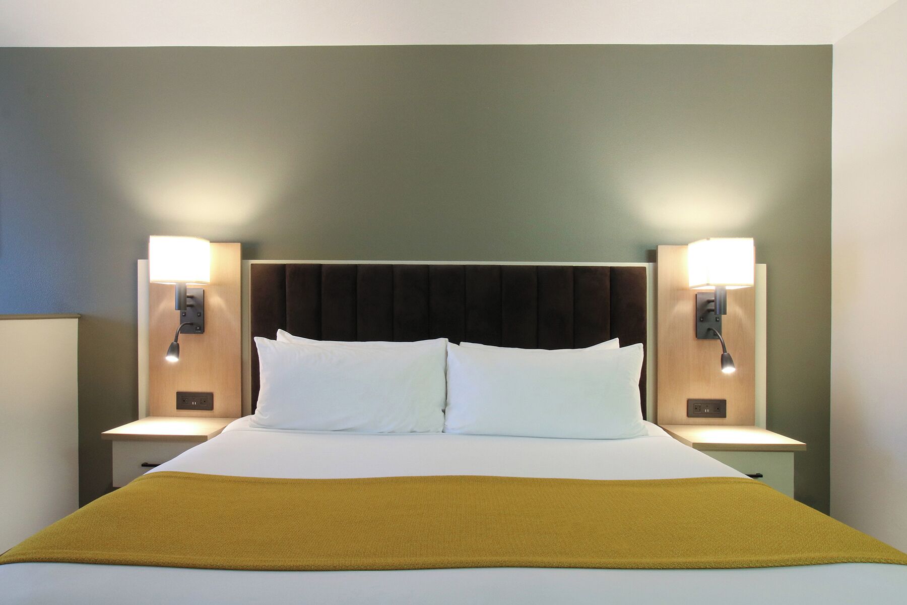 A hotel room with a large bed, two bedside lamps, and a headboard.