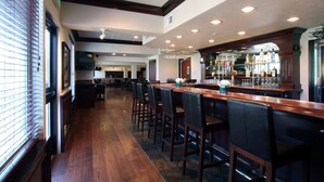 A bar area with wooden bar stools, a long counter, and a well-stocked bar. - Oxford Suites Spokane Valley (Spokane Valley)