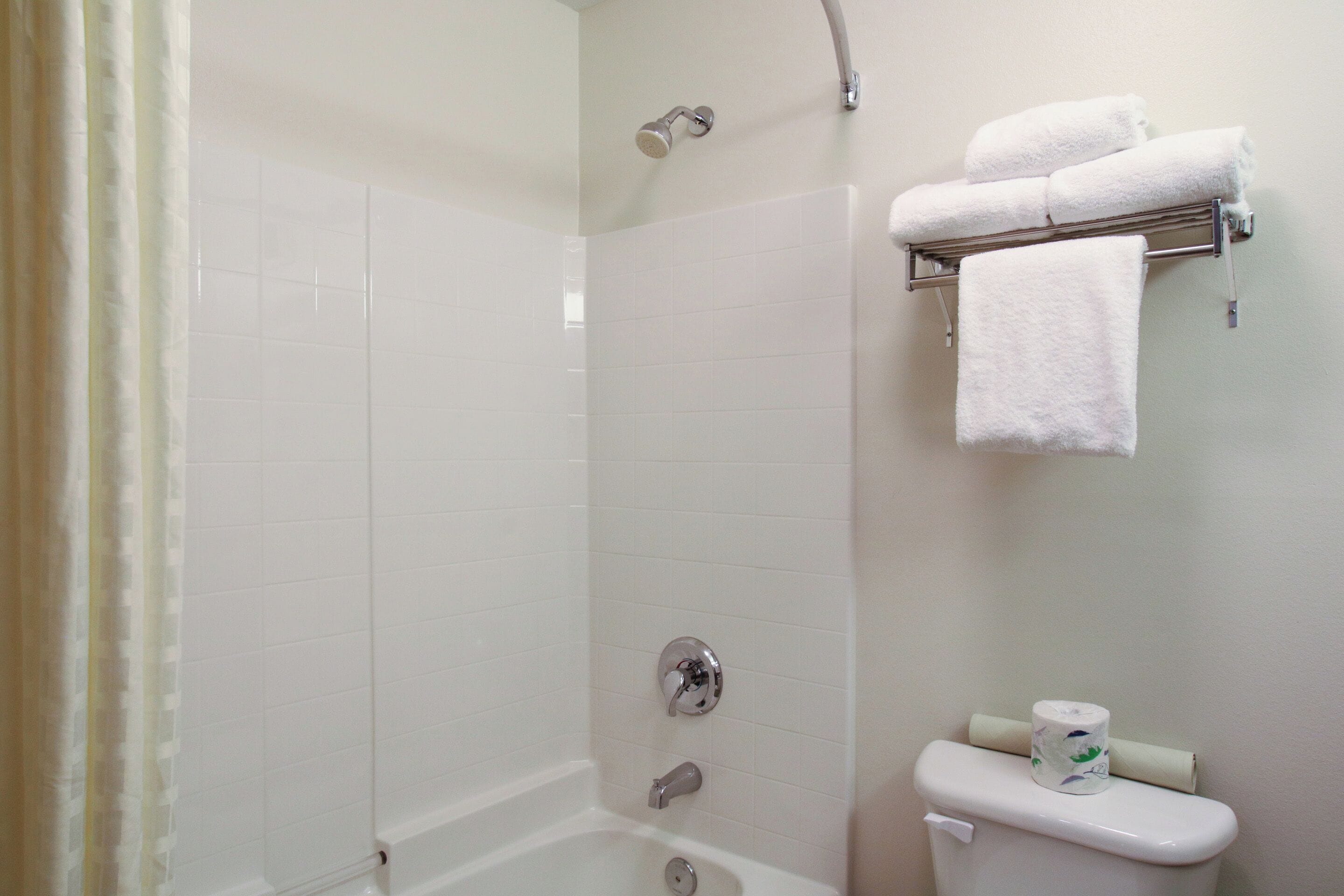 A bathroom with a shower, a toilet, and a towel rack with towels.