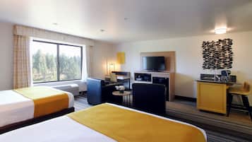 Habitación de hotel con dos camas, un escritorio, televisión y vistas a árboles desde la ventana.