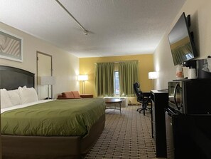 A hotel room with a bed, desk, chair, television, and a microwave.