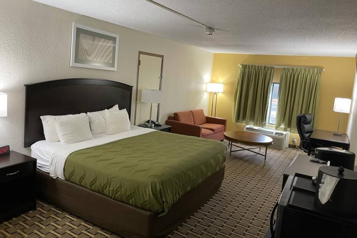 A hotel room with a large bed, a desk, a chair, a lamp, and a window with curtains.