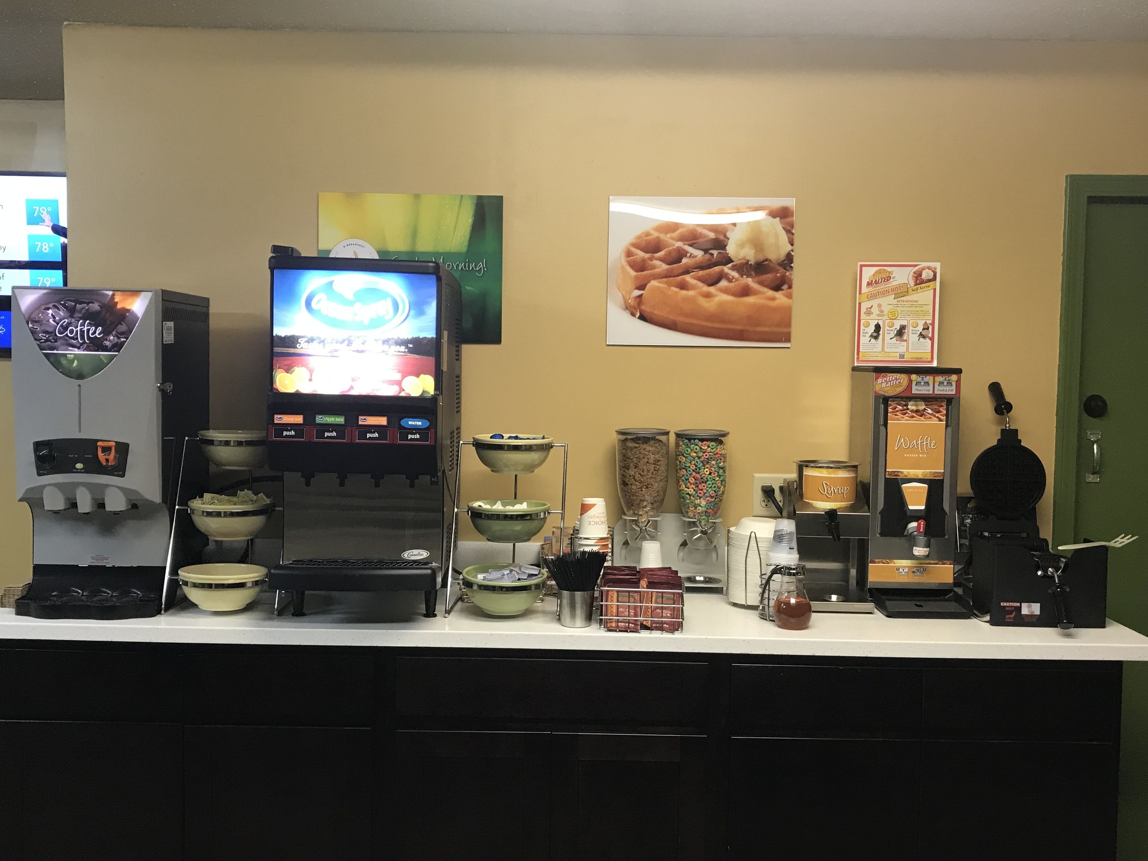 A coffee station with a coffee machine, a waffle maker, and various condiment dispensers.