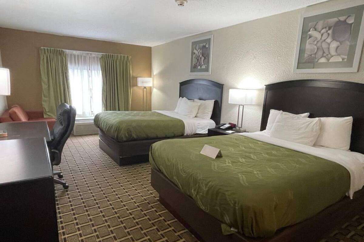 A hotel room with two beds, a desk, a chair, and a window with curtains.